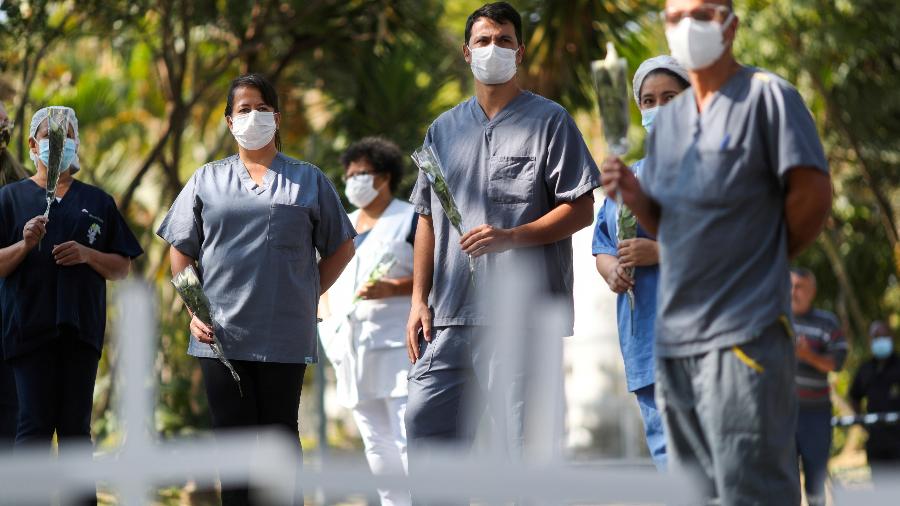 Profissionais de saúde que usam máscaras protetoras seguram flores na frente de cruzes em homenagem à colega de trabalho Maria dos Santos, uma enfermeira que morreu da doença por coronavírus, em meio 